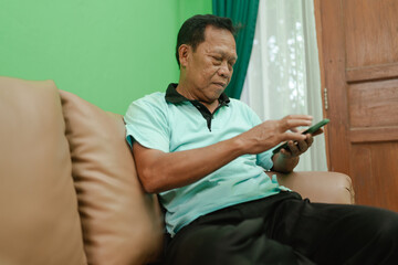 An elderly man is comfortably using his mobile phone while he relaxes indoors in his home