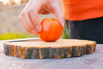tomato on a homemade food cutting board is held by a man's hand