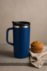 A stylish blue travel mug next to a freshly baked muffin, perfect for a quick breakfast