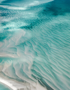 Aerial view of the turquoise sea gently laps against the pale sandy shores, creating an ethereal dance of light and shadow, Moreton Island, Queensland, Australia.