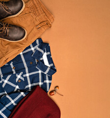 Stylish children’s autumn outfit flat lay with plaid shirt, brown shorts, leather boots and knit...