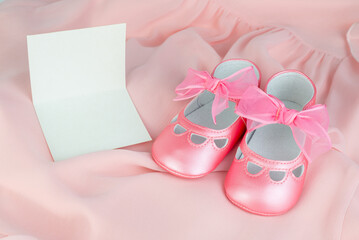 Close-up of adorable pink baby shoes with ribbons on a pink background with a blank gift card
