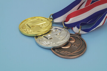 Close up of gold, silver and bronze medals with ribbons on blue background	