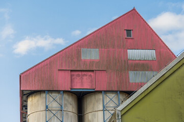 Fototapeta premium Red Industrial Facility with Silos and Structural Frames under Clear Sky