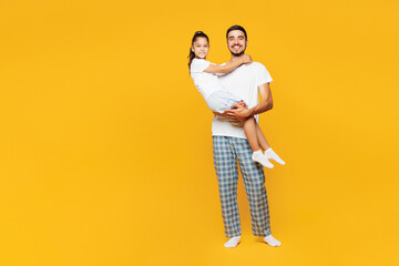 Full body young parent man with child girl wear casual blue pyjamas clothes. Daddy hold little kid daughter in hands look camera isolated on plain yellow background. Father's Day Love family concept.