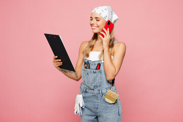 Young laborer handyman woman wear denim overhaul hold clipboard with papers document talk on mobile...