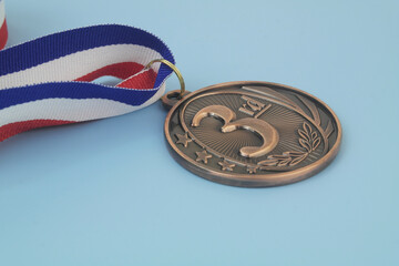 Close up of bronze medal with ribbon on blue background.