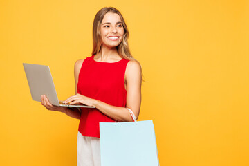 Side view young IT woman in red casual clothes hold shopping paper package bags use work on laptop...