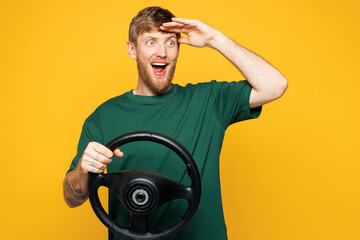 Young shocked Caucasian man he wear green t-shirt casual clothes hold steering wheel driving car...