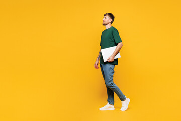 Full body side profile view young IT man wear green t-shirt casual clothes hold closed laptop pc...
