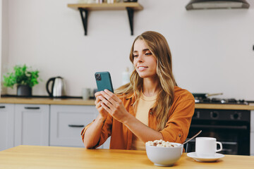 Young smiling happy housewife woman wears orange shirt casual clothes hold in hand use mobile cell...