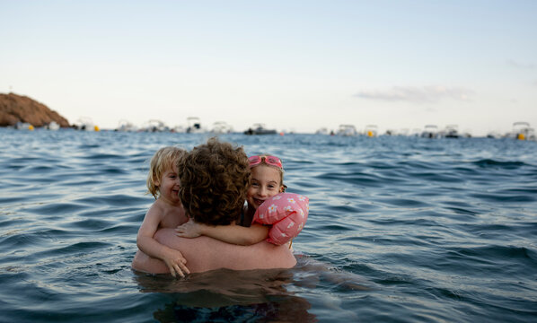 Father hugging children in sea at the beach on a sunny day