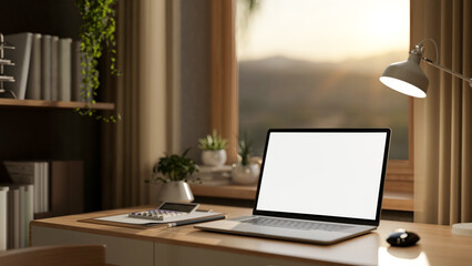 Blank screen laptop with books and calculator on wooden table under window in a sunlit living room.