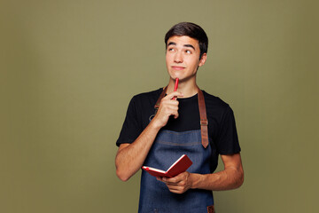 Young minded pensive man barista bartender barman employee wear jeans apron black t-shirt work in...