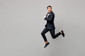 Full body young barista male waiter butler man wears shirt black suit bow tie elegant uniform work at cafe jump high run fast hurry up isolated on plain grey background. Restaurant employee concept.