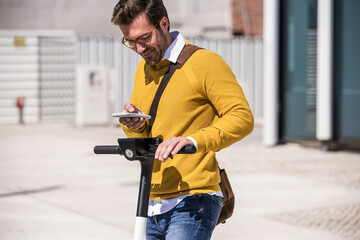 Man in yellow sweater using smartphone on escooter in city