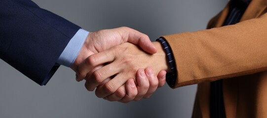 Obraz premium Business partners shaking hands on grey background, closeup