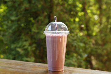 Tasty milkshake in plastic cup on wooden table outdoors