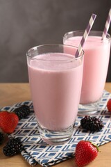 Tasty milkshakes in glasses and berries on wooden table, closeup