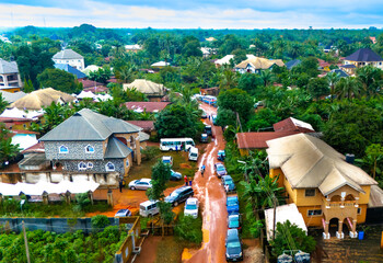 Aerial view of vehicles parked on a street lined with buildings, surrounded by lush greenery, evoking a sense of vibrant life, Okwele Community, Imo State, Nigeria.