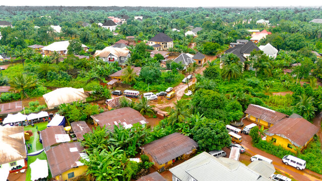 Aerial view of a Okwele Community with cars and buses amidst lush green vegetation and buildings with a mix of corrugated iron and modern roofs, Okewle Community, Imo State, Nigeria.