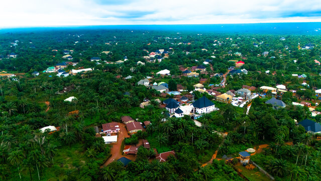Aerial view of dense green canopy interspersed with buildings under a vast sky, a tapestry of nature meeting civilization,  Okwele Community, Imo State, Nigeria.