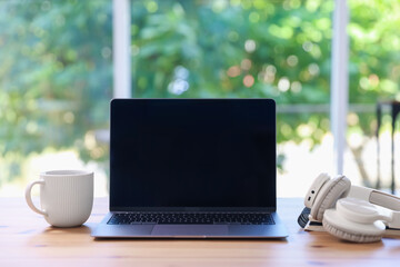 Fototapeta premium Home workspace. Laptop, cup of drink and headphones on wooden desk near window indoors