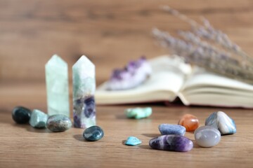 Different healing stones and book on wooden table, closeup