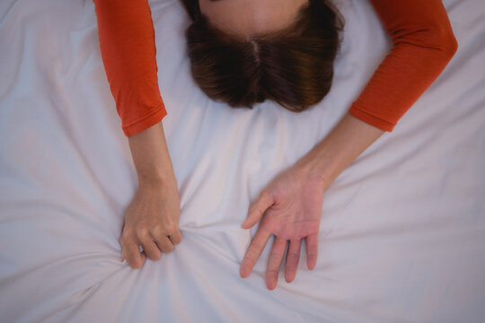 Woman lying face down on bed, gripping the sheets tightly, experiencing a nightmare. Top view captures the intensity of her struggle against fear and anxiety during sleep