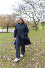 Fototapeta premium Senior woman walking in park with folded umbrella on cloudy day