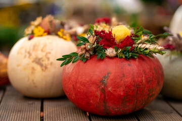 View of ripe pumpkins decorated with colorful flowers. Halloween decor. Holiday decor with pumpkins and flowers