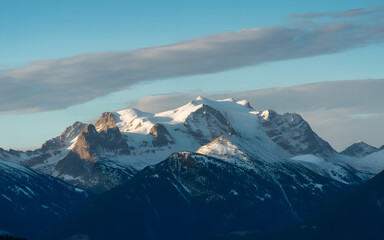 Majestic snow-capped mountain peak bathed in golden sunlight under a clear blue sky with wispy clouds