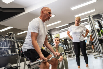 Two elderly couples exercise together with guidance from a young female instructor at the gym,...