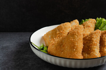 Close up Risol Mayo segitiga or Triangle Risol mayonnaise served in a white bowl with fresh lettuce and green chili on dark background. Showcasing a savory Indonesian snack with breadcrumb coating. 