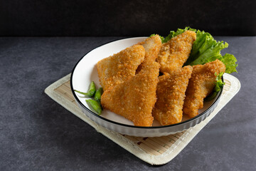 Risol Mayo segitiga or Triangle Risol mayonnaise served in a white bowl with fresh lettuce and green chili on dark background. Showcasing a savory Indonesian snack with breadcrumb coating. 