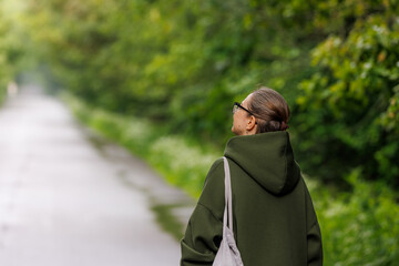 Woman enjoying a peaceful walk along a serene path surrounded by lush greenery in early afternoon light