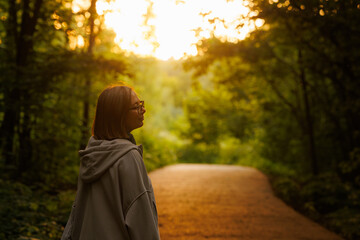 Woman enjoys a peaceful moment on a forest path during sunset surrounded by vibrant greenery