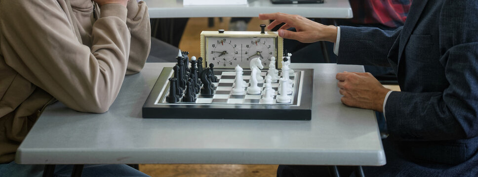 Grandmaster in a suit hits the chess clock after a move against an opponent; time pressure and strategy drive the duel—business‑style decision for gain. Photo