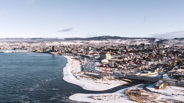 Hyperlapse zoom in aerial view of Punta Arenas coastline in Chile, with snow covering the city and shore.