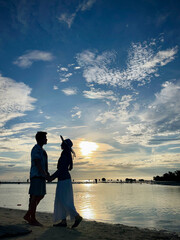 Fototapeta premium Silhouette of a romantic couple holding hands by the beach at sunset, facing each other with scenic ocean and colorful sky background