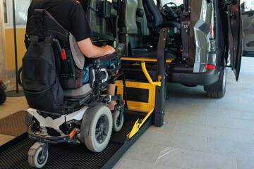 Person with disability is using a wheelchair ramp to enter a vehicle at a transportation facility during daytime for mobility assistance.
