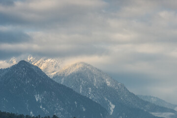 Snowy mountain peak with mist and dramatic clouds in Himalayas. Scenic Himalayan mountain landscape with snow-covered peaks, pine forest, and clouds drifting across the ridges. 