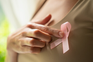 Detailed focus on pink awareness ribbon pinned to shirt with hand touching it, symbolizing support...