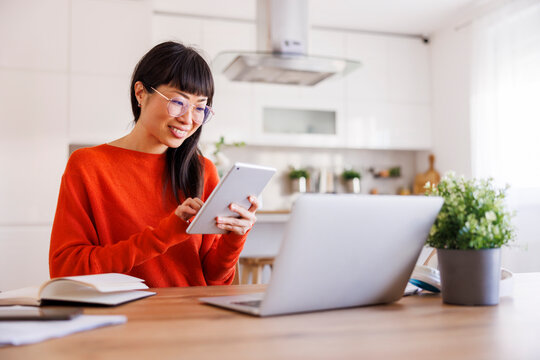 Woman using tablet and laptop computers while working remotely from home - Powered by Adobe