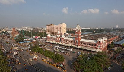 Aerial view of the vibrant red and white brick Chennai Central Railway Station contrasting against the bustling city streets and lush greenery, Chennai, Tamil Nadu, India.