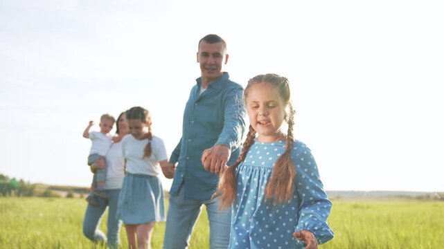 Family walk in green meadow and open field with father and mother holding hands with daughter and son and child nearby while summer sunlight fills grass and smiles showing joy love and playful bond