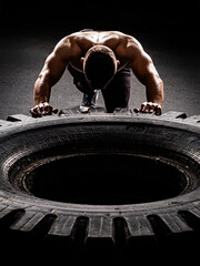 A man with a handsome body pushes a huge wheel. The muscles of the shoulders and back are clearly visible.