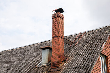 Close-up of a sloped roof with weathered corrugated sheets, a tall red brick chimney, metal flue,...