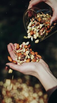 Hand pouring mixed nuts almonds cashews pistachios walnuts hazelnuts sunflower seeds from glass cup into palm healthy organic snack natural protein energy food close up lifestyle nutrition vegan veget