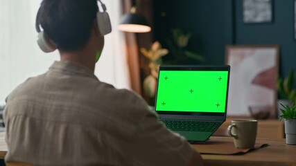 Back view of male freelancer greeting colleagues during video call sitting in front of wireless laptop in modern home office, green chroma key screen, copy space - Powered by Adobe